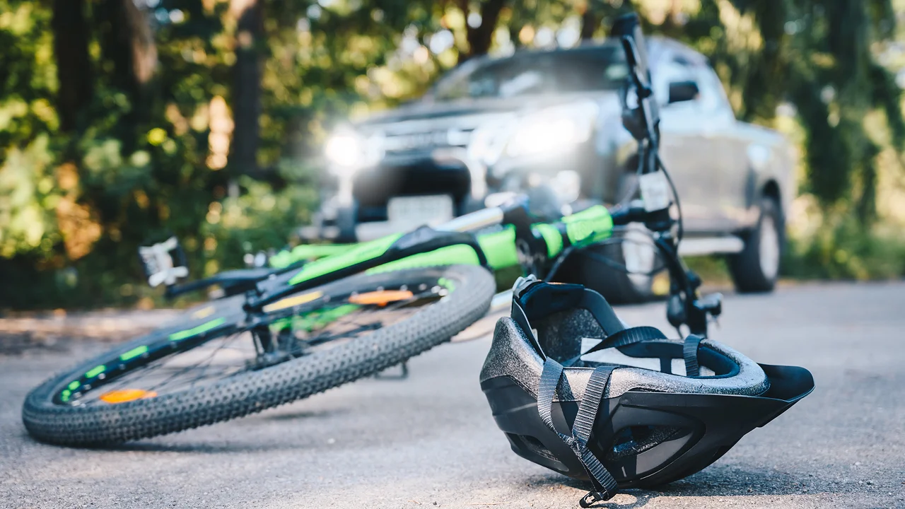 a bicycle and a helmet lie on the ground in the foreground, with a vehicle's headlights visible in the background.