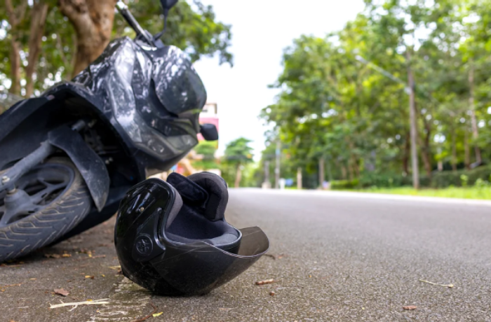 A blurred close-up of a black motorcycle helmet lying on the ground next to a motorcycle after an accident on a suburban road.