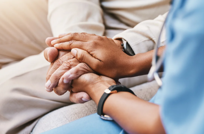 a younger person in blue medical attire provides comfort by gently holding the hands of an older individual.