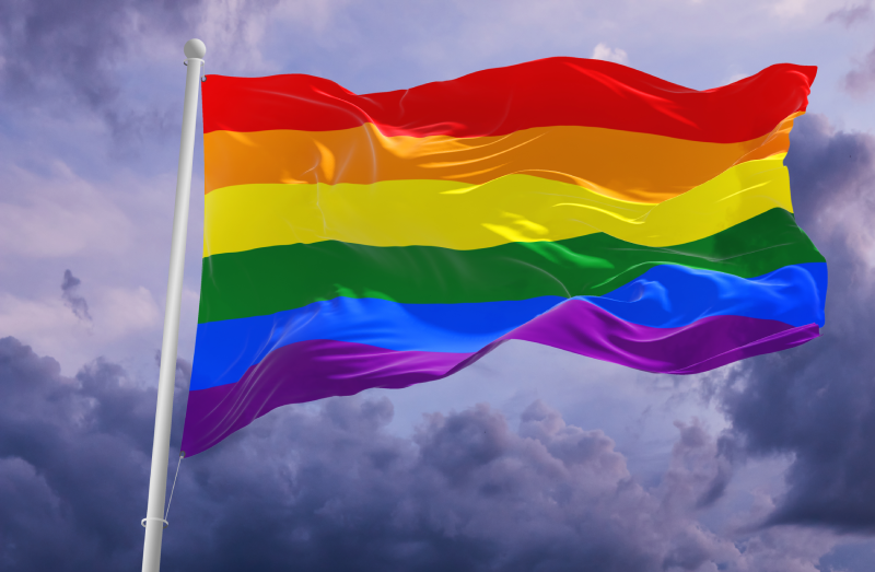 Pride rainbow lgbt gay flag being waved in the breeze against a sunset sky.