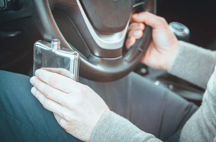 A man is driving a car, holding a bottle of alcohol in one hand and the steering wheel in the other. Road safety concept