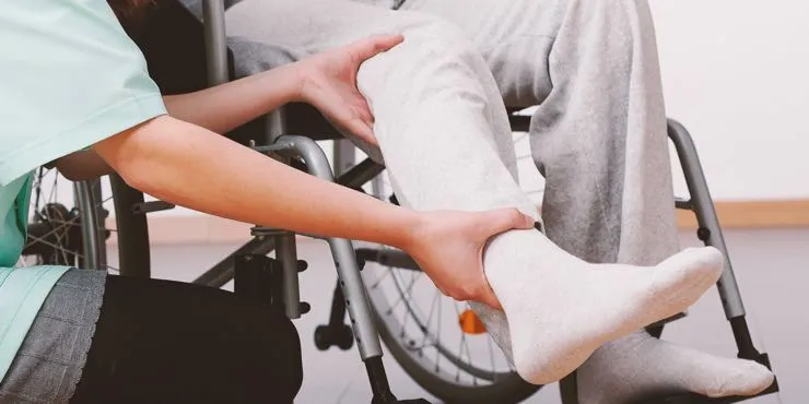A healthcare worker assists a person in a wheelchair by gently lifting and supporting their leg.