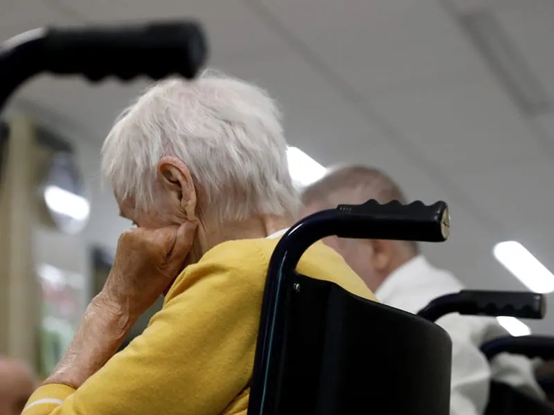 Gemini said An elderly person with white hair sits in a wheelchair, seen from behind, with their hand resting on their face.
