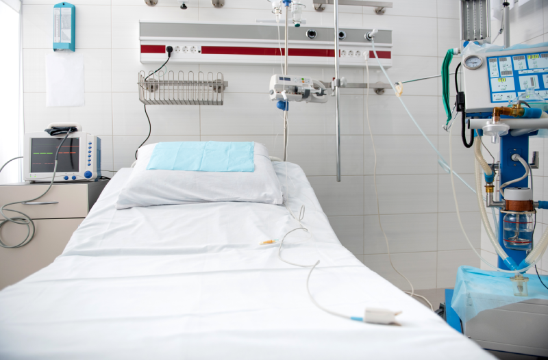 Hospital bed with sterile sheets and pillow surrounded by breathing apparatus and digital device for measuring blood pressure