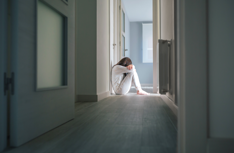Unrecognizable woman with mental disorder in pajamas sitting on the floor of a mental health center