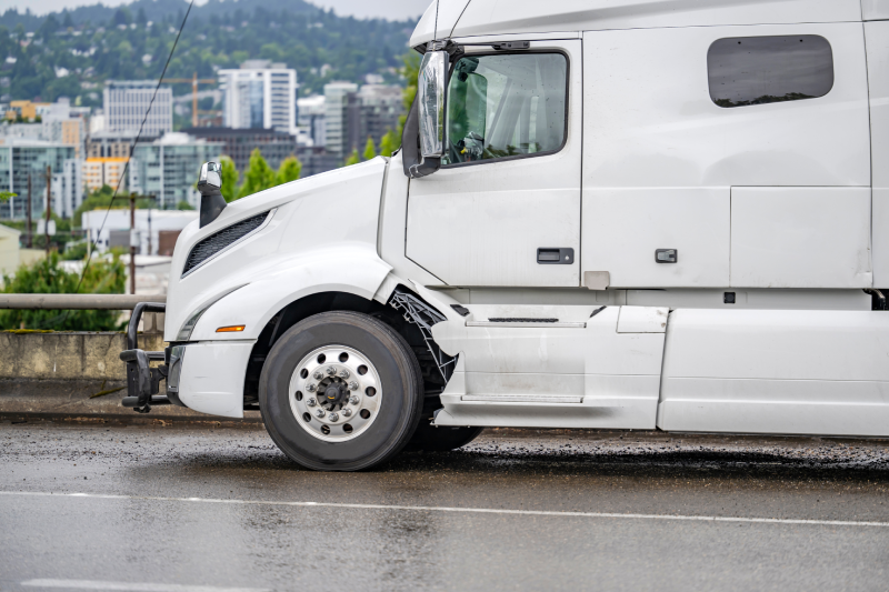 Broken after an accidental collision big rig semi truck tractor with body damage standing out of service on the highway road shoulder waiting for road assistant mobile towing truck for help