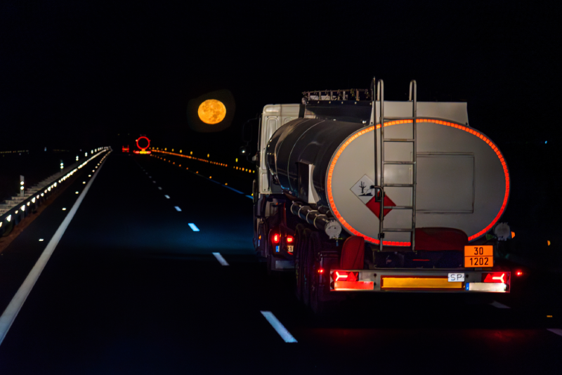 Tanker truck with danger plates, transporting fuel, driving at night on the highway with the full moon in the background