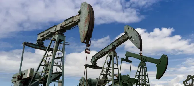 several large, green pumpjacks are shown operating under a bright blue sky with scattered white clouds.