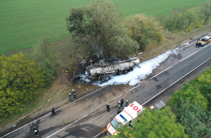 Top aerial view. The fuel truck crashed into a tree and caught fire. Fire truck and ambulance came to the rescue