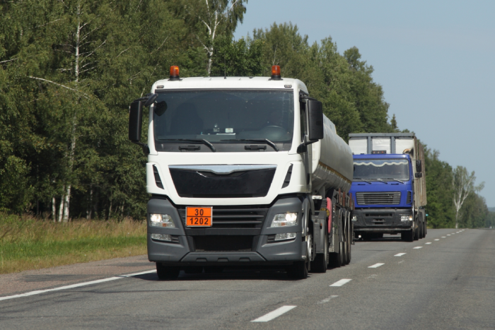 Diesel transportation, white fuel tank truck with ADR sign 30 1202 on suburban asphalted road at Sunny summer day on blue sky and green trees background, flammable liquid goods transportation