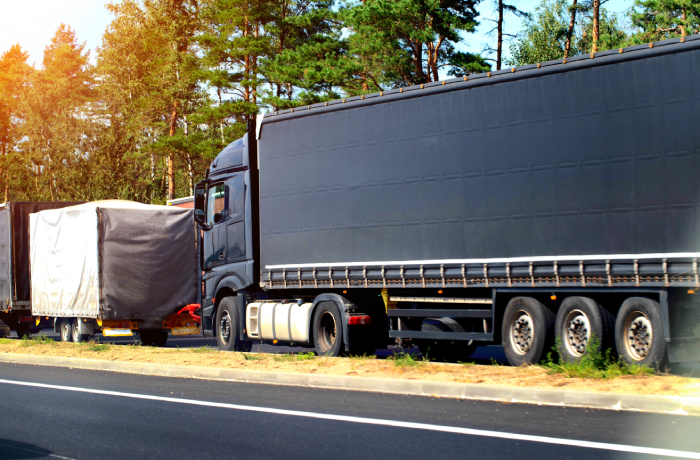 A black semi-trailer truck crashed into the trailer of another vehicle on the road.