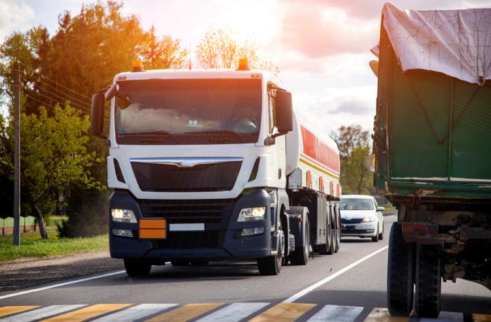 Modern truck with tank trailer transports dangerous cargo acetone and oil against cloudy sky and sun. Fire hazard class