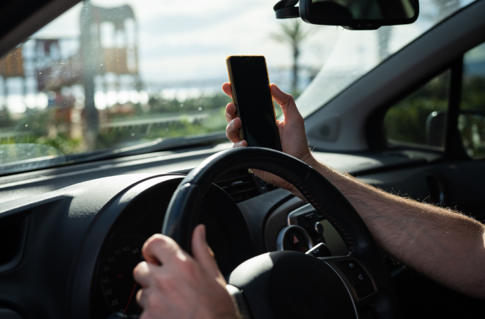 Man driving a car while using a smartphone, representing the danger of distracted driving and lack of attention on the road.