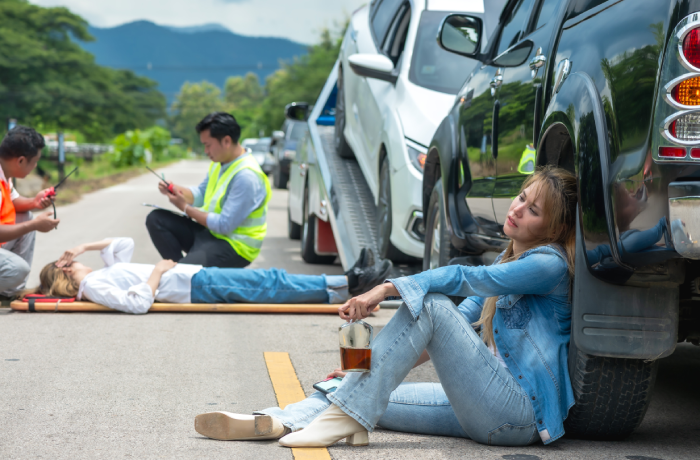 Drunk driver woman holding alcohol bottle sitting with accident scene background