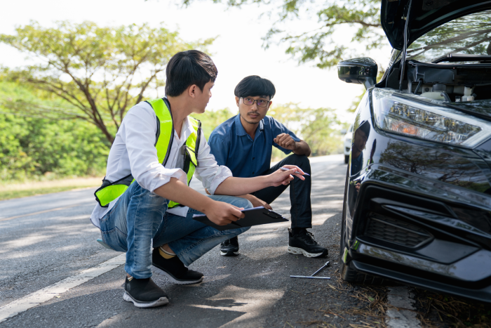 Mechanic or driver providing roadside assistance by changing a flat tire and performing minor repairs on the side of the road during a vehicle breakdown.