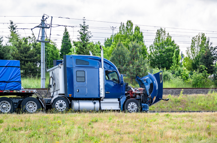 Accidentally broken down while driving blue big rig semi truck with open hood and loaded flat bed semi trailer stands on the highway