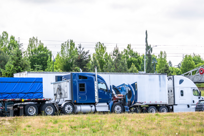 Broken blue big rig semi truck tractor with open hood and loaded flat bed semi trailer standing on the road shoulder out of service waiting for mobil road assistant towing or repair team for help